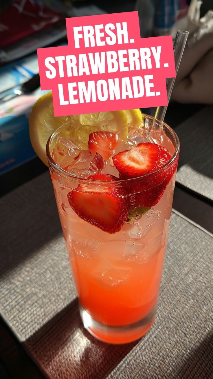 A refreshing glass of strawberry lemonade with ice and a lemon slice